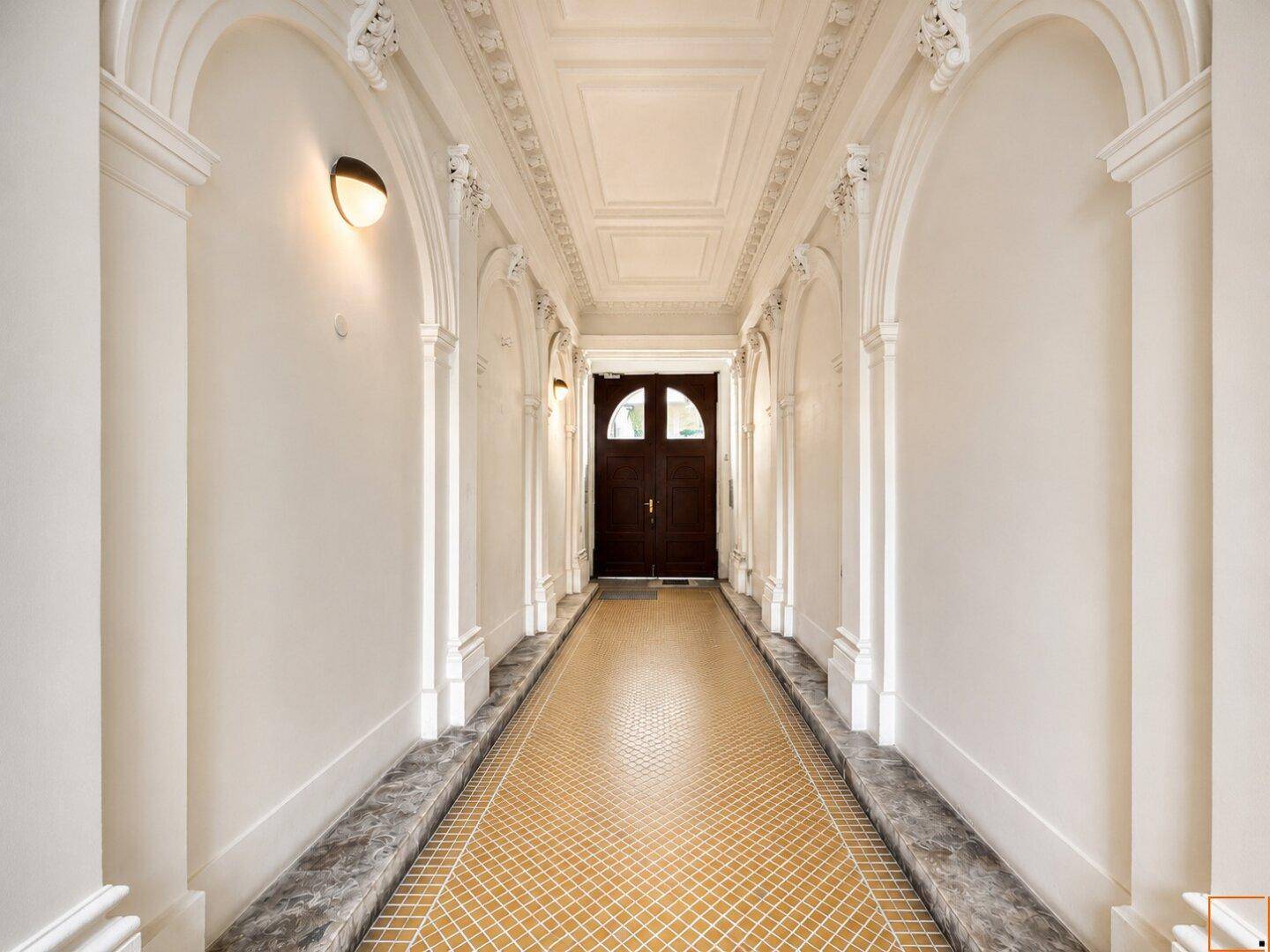 Eleganter Flur mit verzierten Bögen, Stuckdecke und einem gemusterten Fliesenboden im Altbau.