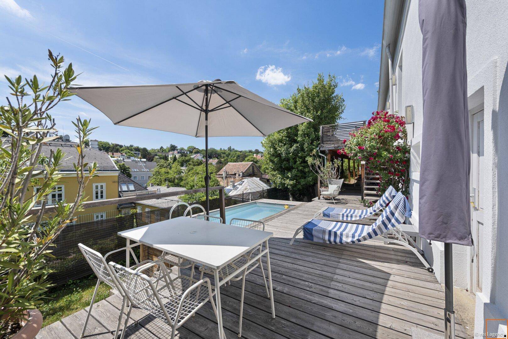 Sonnige Terrasse mit Esstisch, Sonnenschirm und kleinem Pool mit Stadtblick.