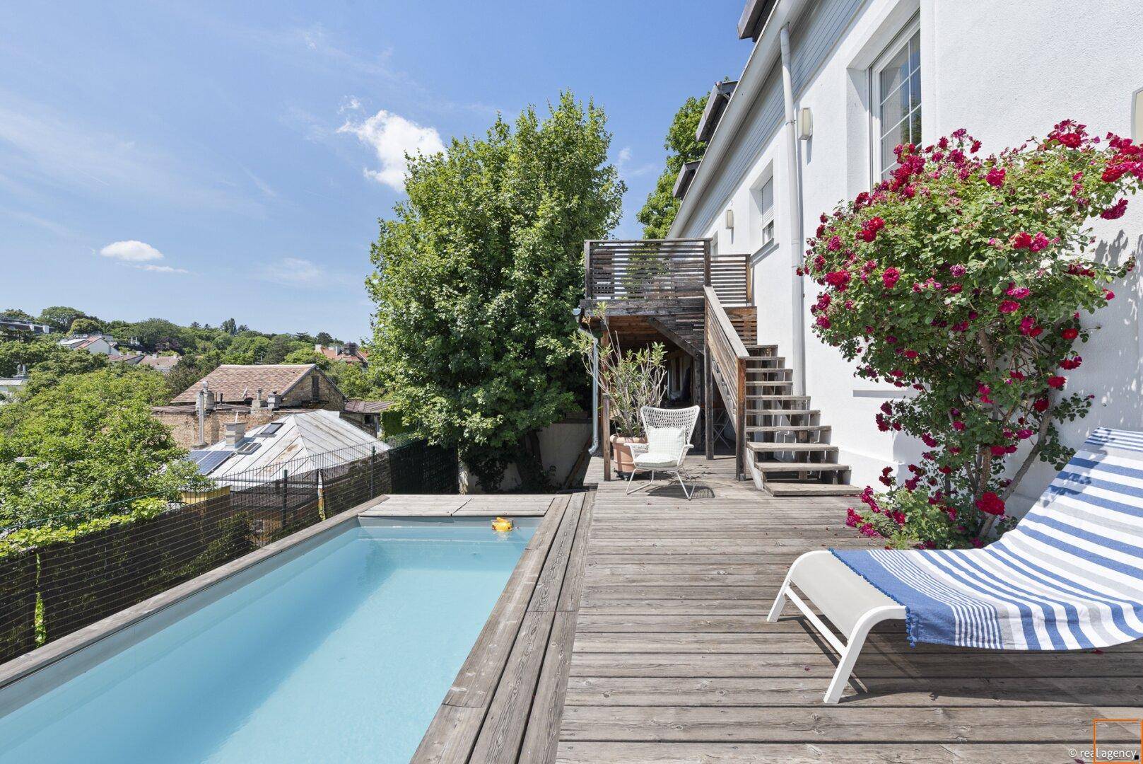 Holzterrasse mit langem Pool, Sonnenliegen und blühenden Rosensträuchern.