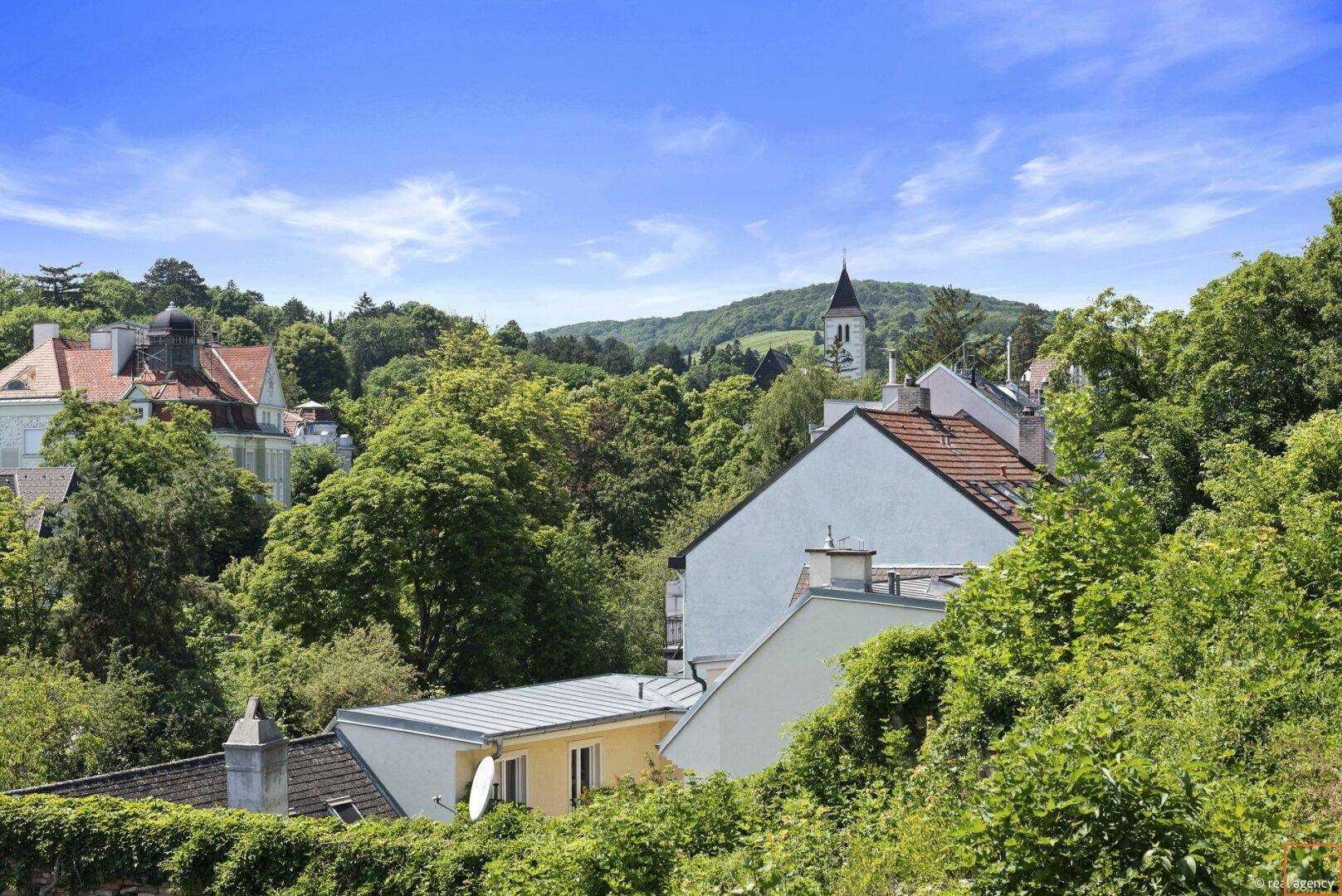 Panoramablick über eine grüne Hügellandschaft mit Häusern und Kirchturm.
