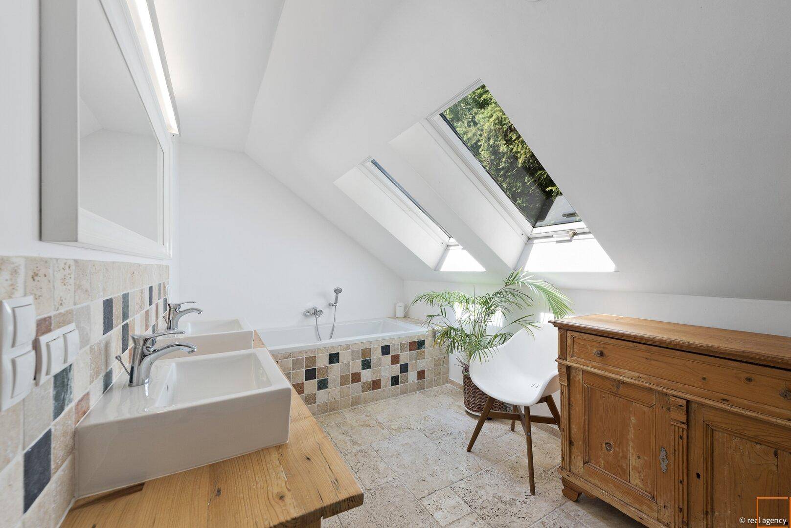 Modernes Badezimmer im Dachgeschoss mit Badewanne, Doppelwaschbecken und Dachfenstern.
