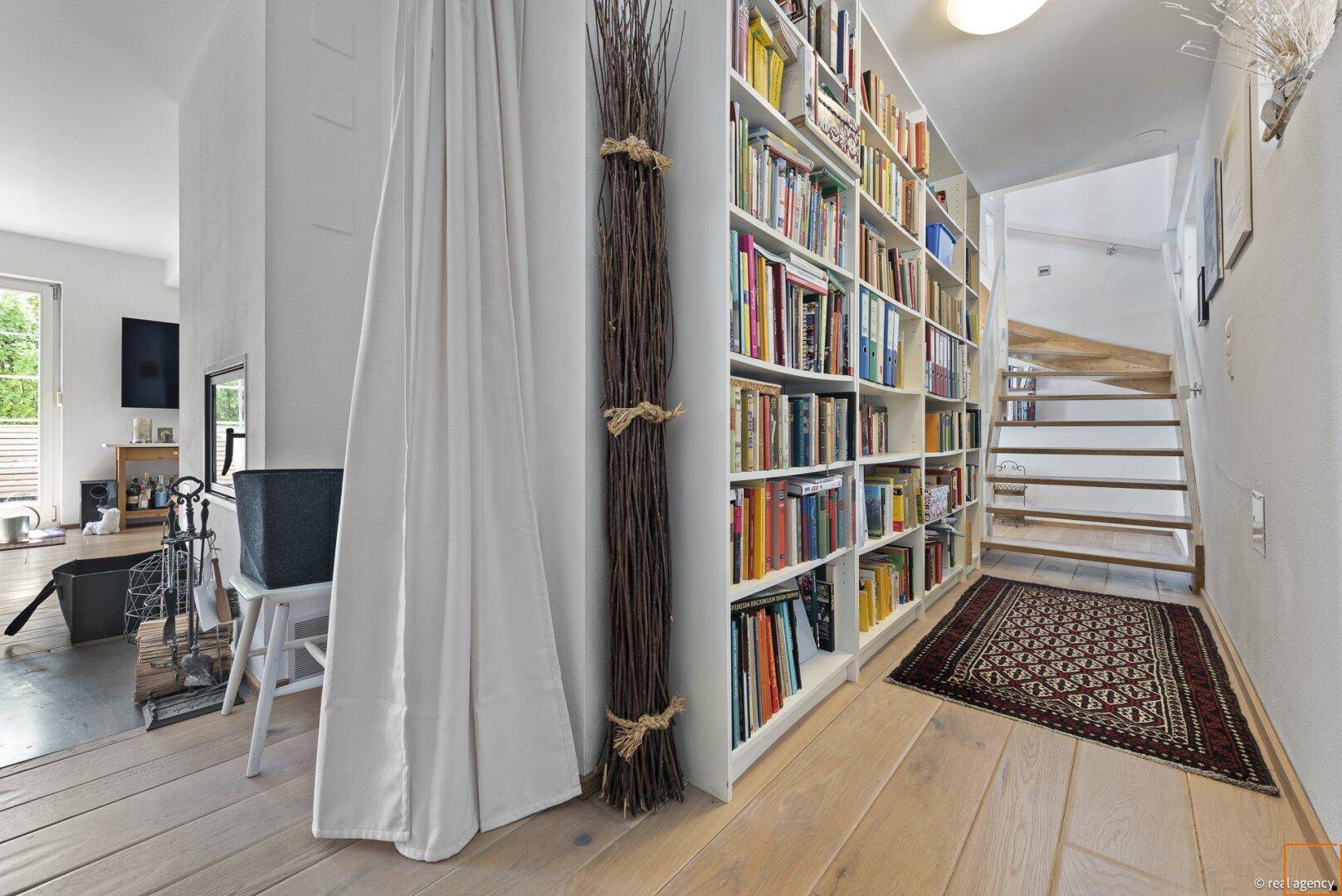 Heller Flur mit großer Bücherwand, Holzboden und Treppe zum Obergeschoss.