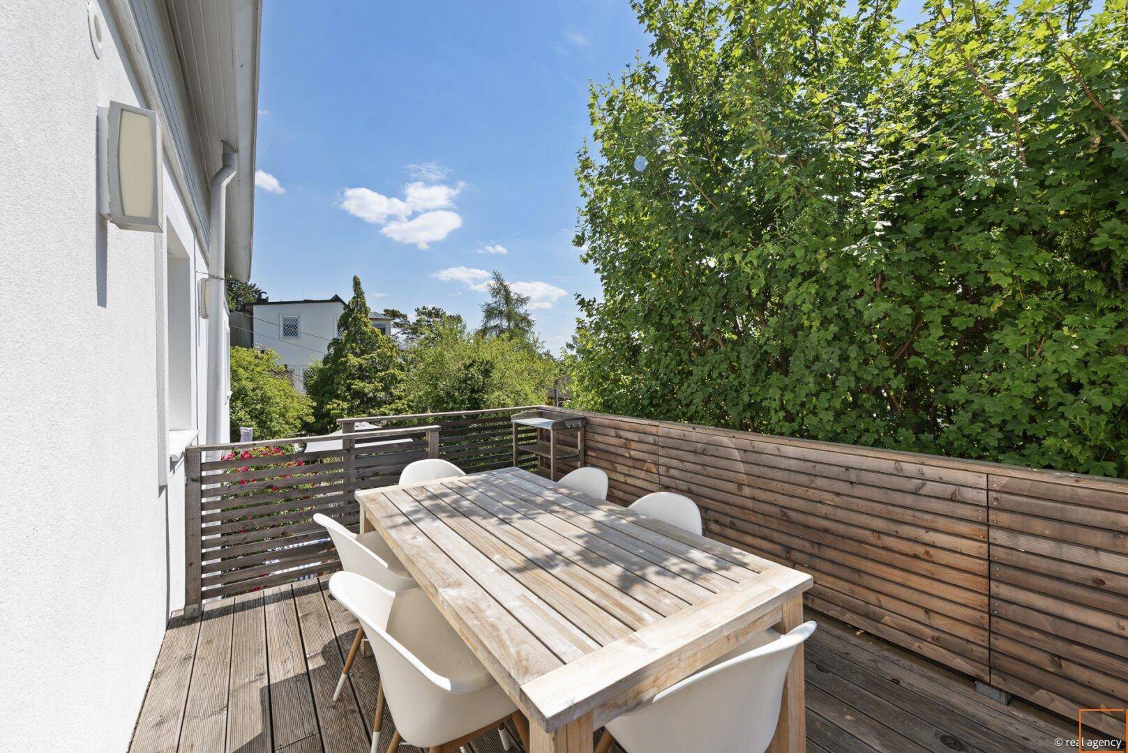 Holzterrasse mit Essbereich und Blick auf üppiges Grün und Bäume.