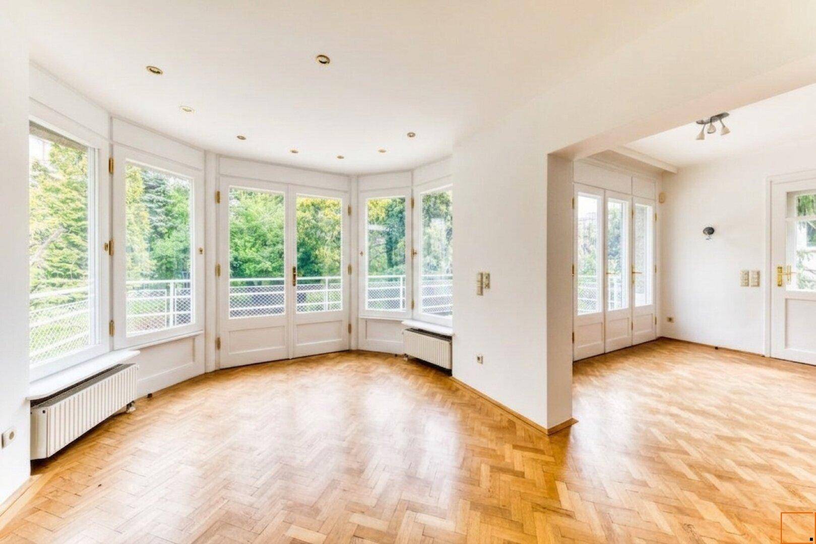 Geräumiges Wohnzimmer mit vielen Fenstern und klassischem Fischgrätparkett.