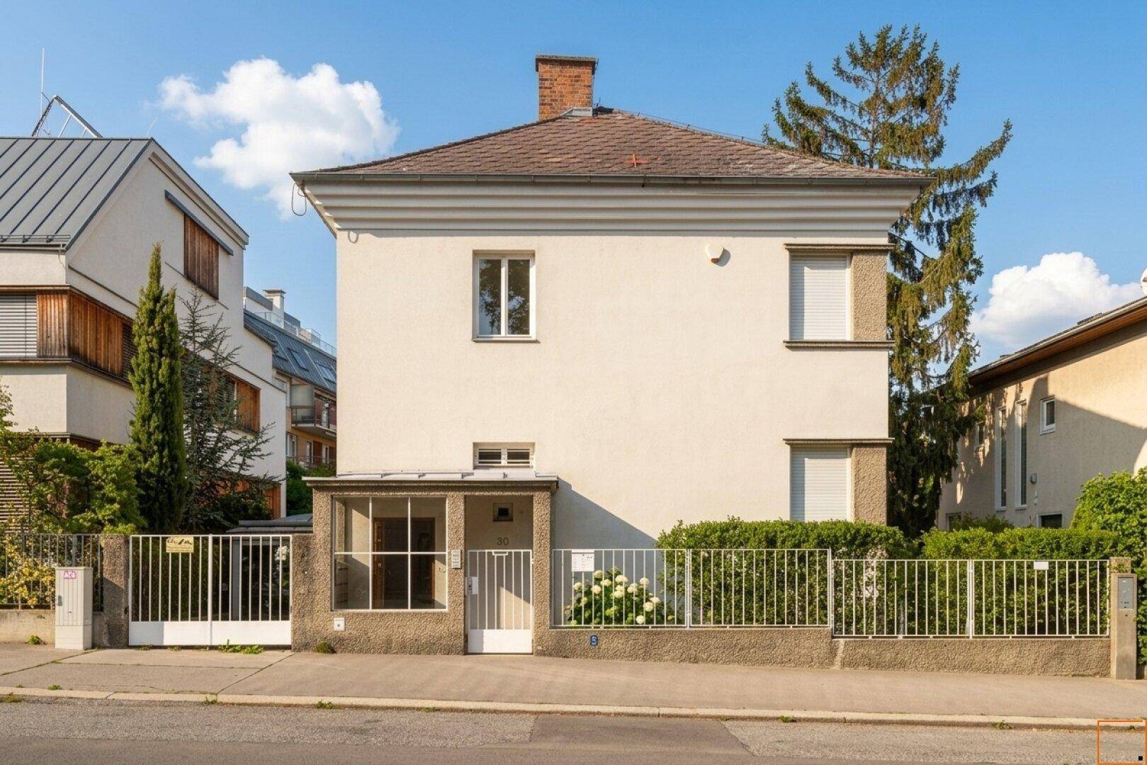 Klassische Hausfassade mit gepflegtem Vorgarten und Zaun zur Straße.