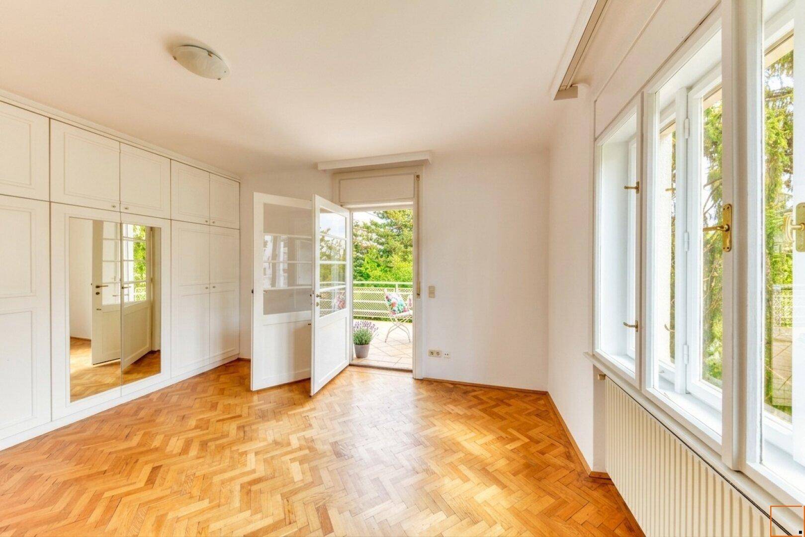Schlafzimmer mit Einbauschränken, Fischgrätparkett und Zugang zu einem kleinen Balkon.