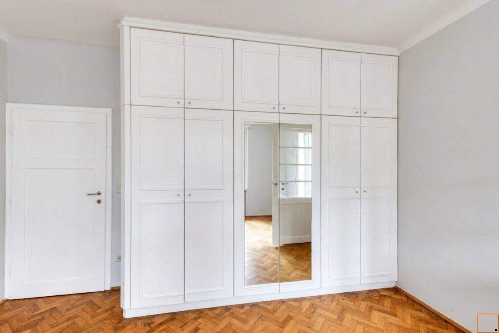 Geräumiges Schlafzimmer mit großen weißen Einbauschränken und Spiegel.