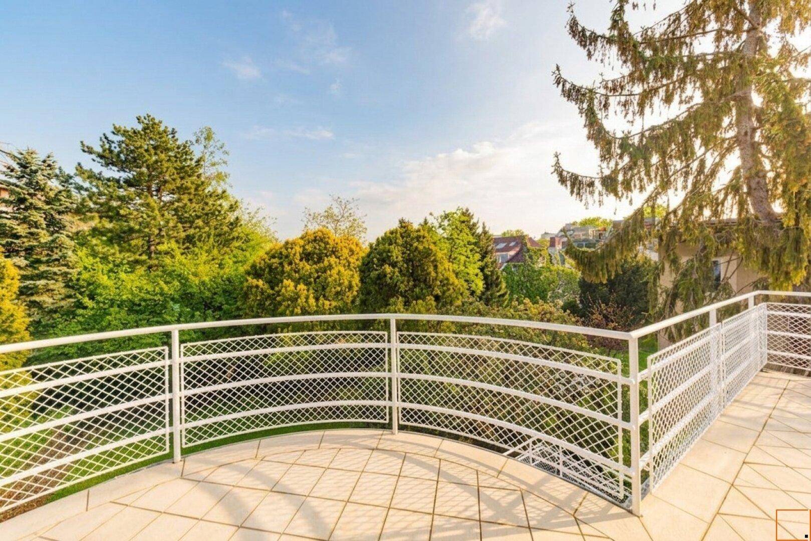 Großer, sonniger Balkon mit weißem Geländer und weitem Blick ins Grüne.