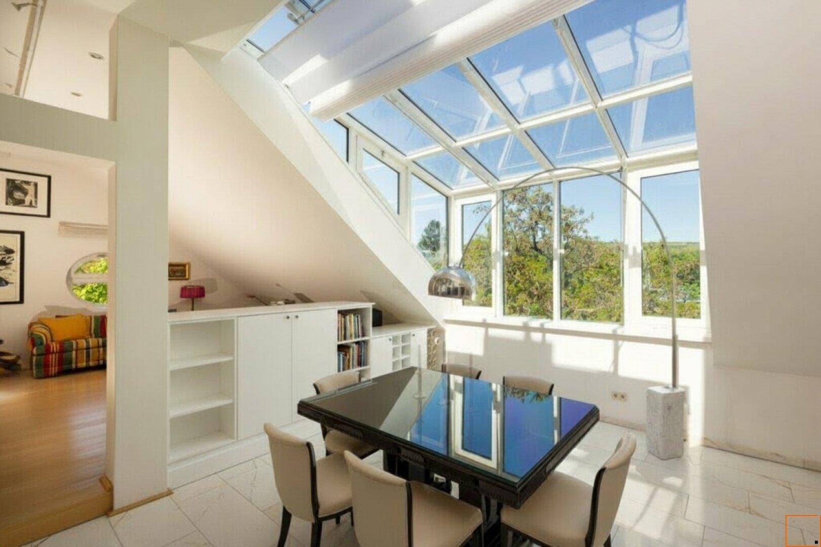 Helles Esszimmer mit großem Glastisch, umgeben von schrägen Dachfenstern und Blick ins Grüne.