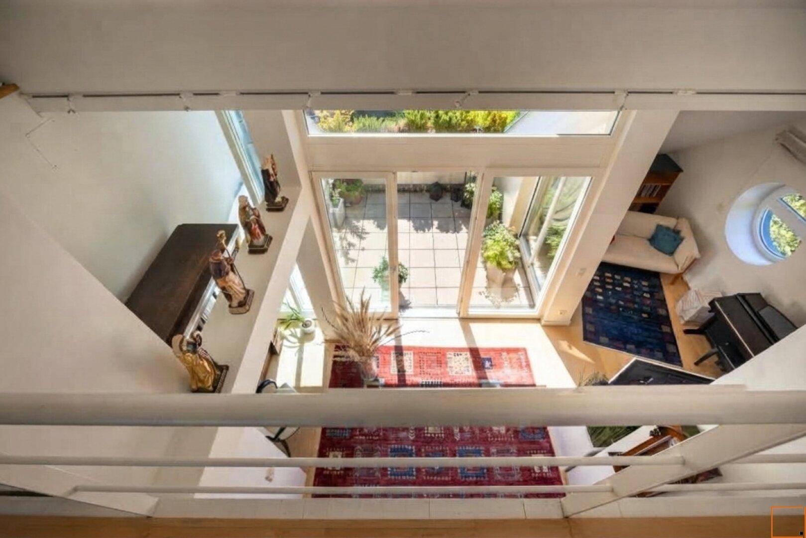 Blick von oben in einen offenen Wohnbereich mit Zugang zu einer sonnigen Terrasse und runden Fenstern.