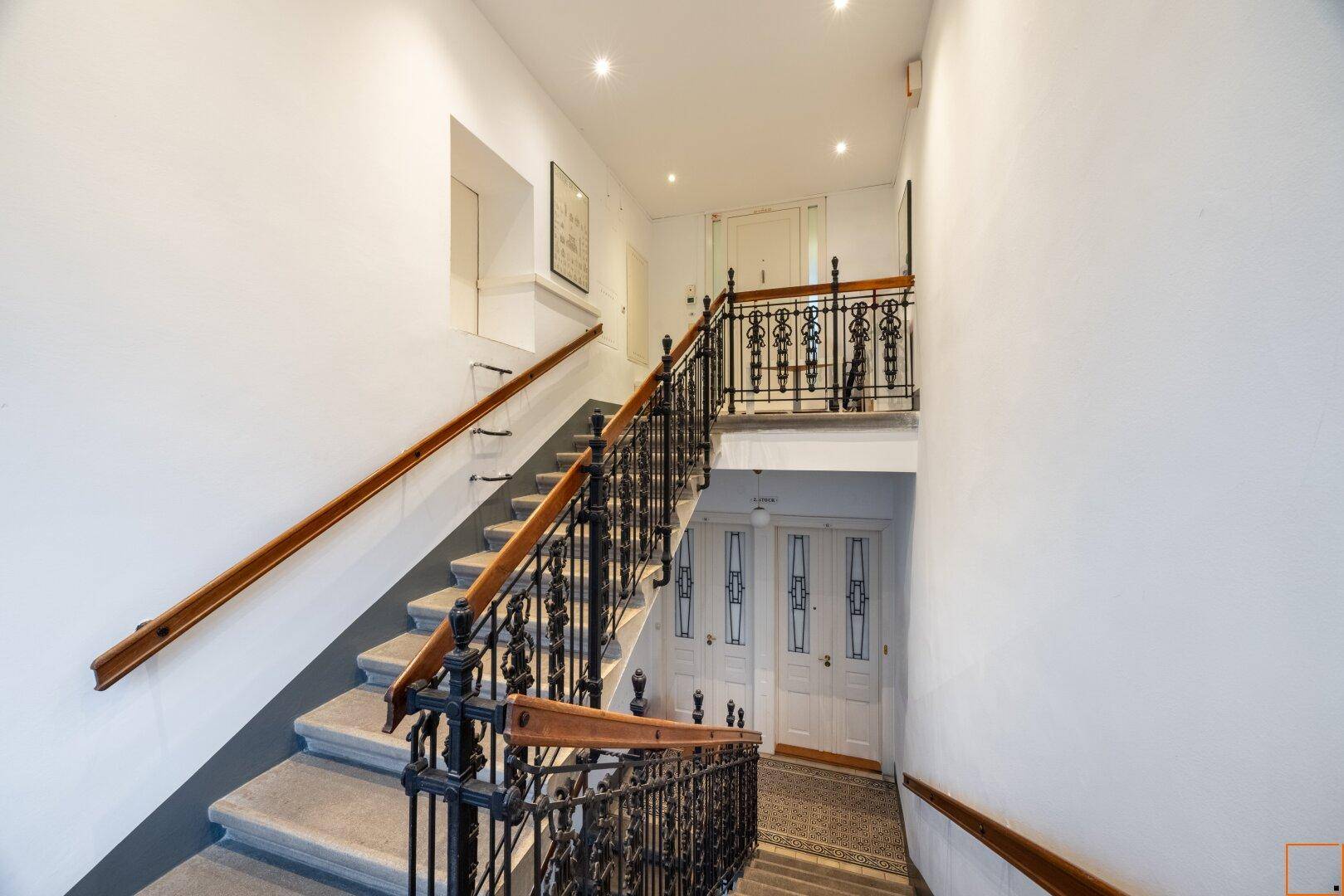 Elegantes Treppenhaus mit schmiedeeisernem Geländer und Holzhandläufen in einem hellen Eingangsbereich.