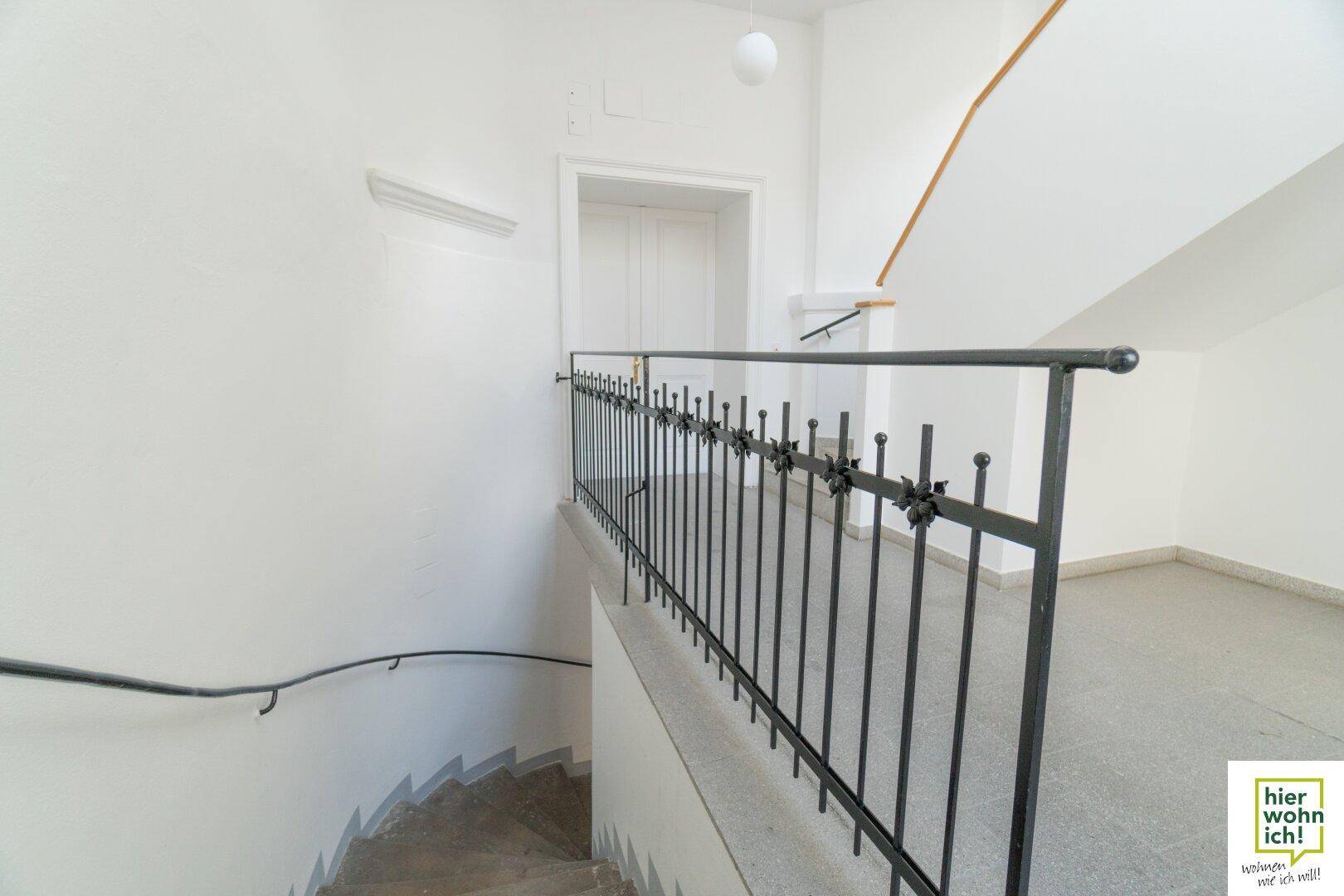 Treppenhaus mit Steinstufen, schmiedeeisernem Geländer und Zugang zu den oberen Etagen.