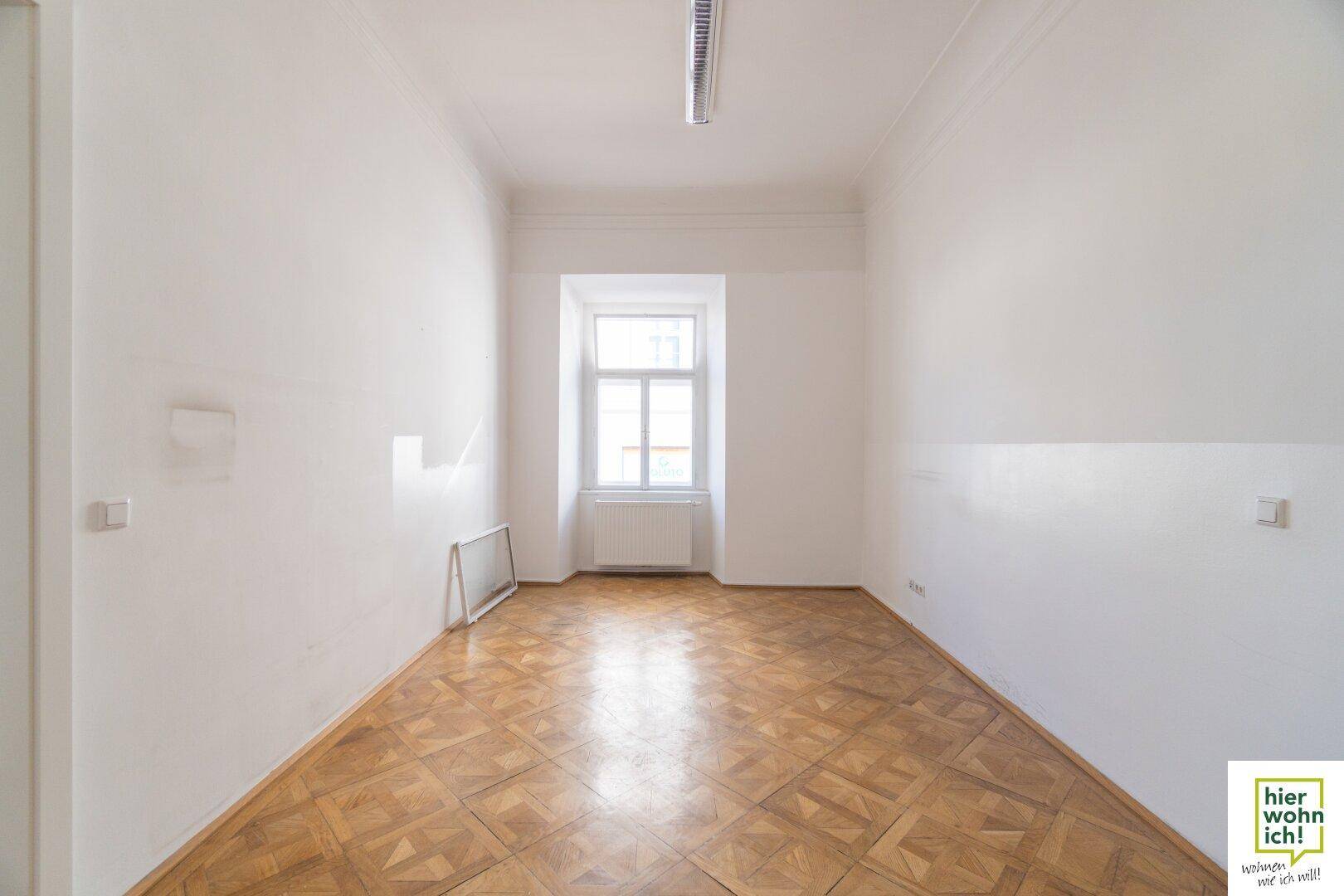 Heller Raum mit Fischgrätparkett und einem Fenster, das viel Tageslicht hereinlässt.