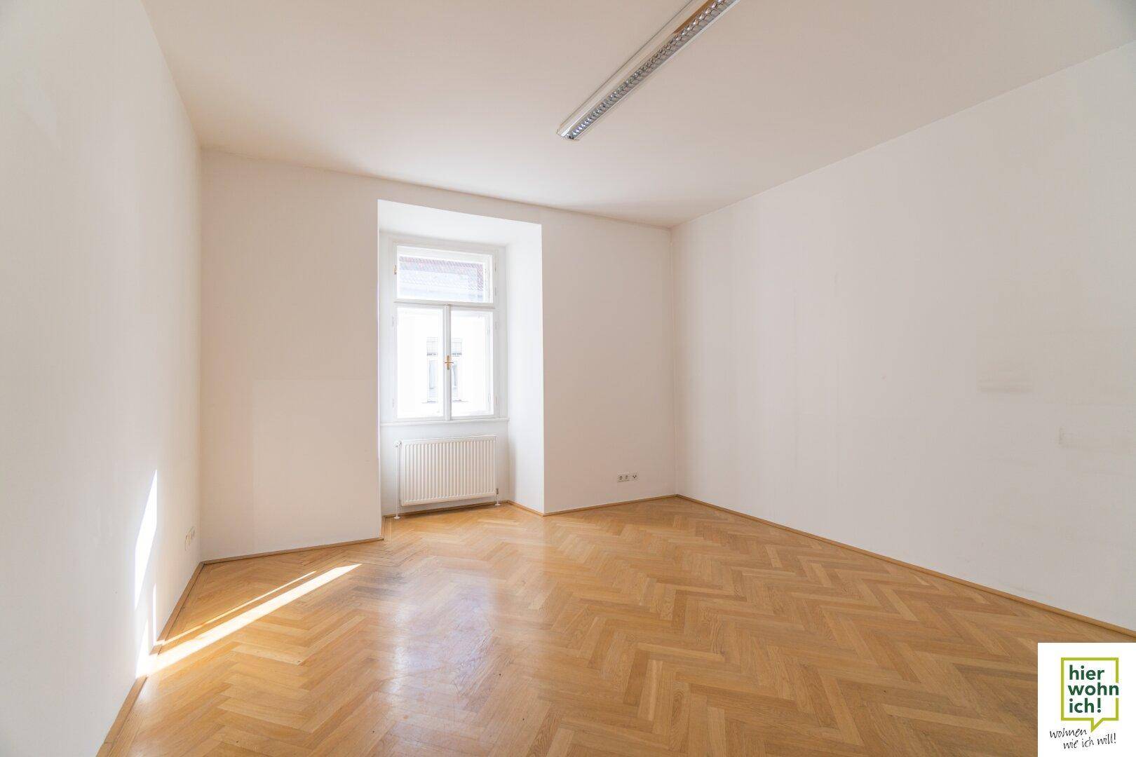 Heller Raum mit Fischgrätparkett und einem Fenster, das viel Tageslicht hereinlässt.