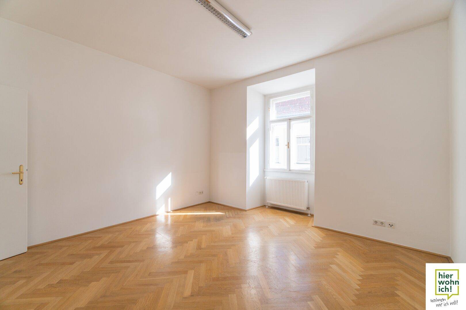 Heller Raum mit Fischgrätparkett und einem Fenster, das viel Tageslicht hereinlässt.