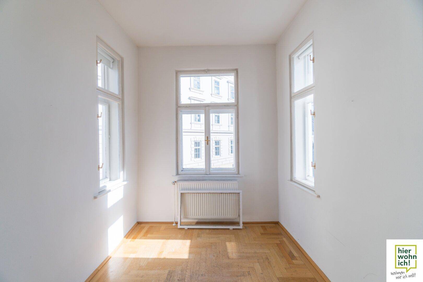 Heller Raum mit Fischgrätparkett und einem großen Fenster, das viel Tageslicht hereinlässt.