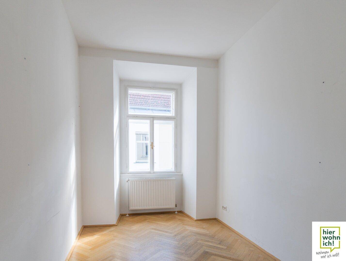 Heller Raum mit Fischgrätparkett und einem Fenster, das viel Tageslicht hereinlässt.