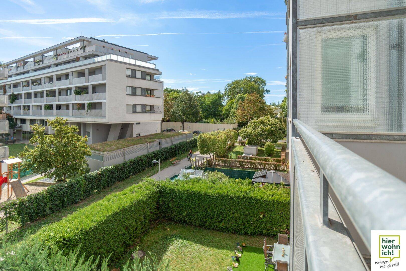 Aussicht vom Balkon auf die gepflegte Gartenanlage mit Sitzgelegenheiten und weiteren Gebäuden.