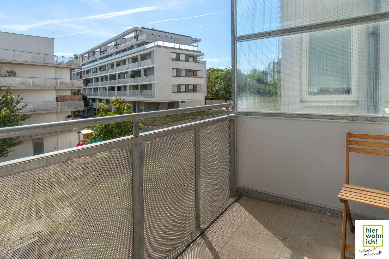 Gemütlicher Balkon mit Sitzgelegenheit und Blick auf die umliegenden Wohngebäude und Grünflächen.