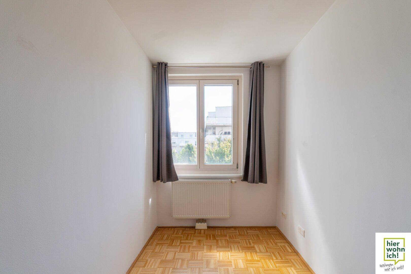 Helles Zimmer mit Parkettboden und großem Fenster, ideal als Kinderzimmer oder Arbeitsbereich.