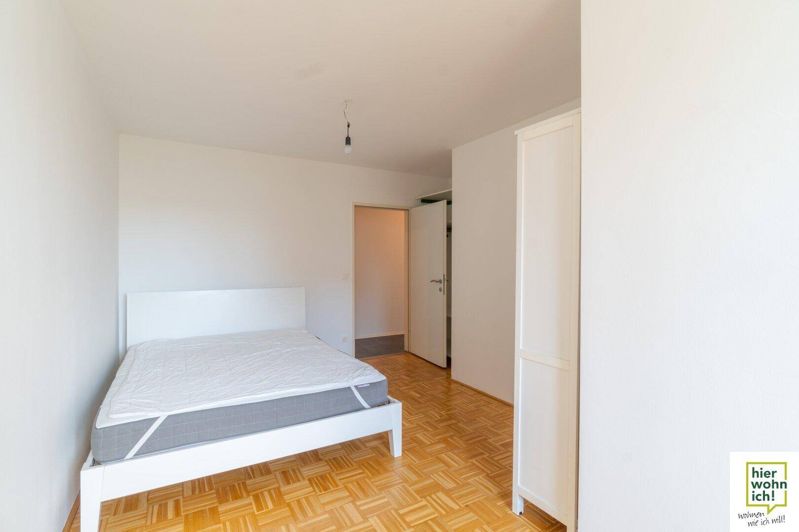 Schlafzimmer mit Parkettboden, Bett und Kleiderschrank, bietet direkten Zugang zu einem weiteren Raum.