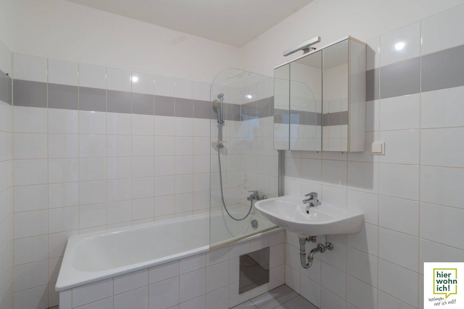 Modern gefliestes Badezimmer mit Badewanne, Waschbecken und Spiegelschrank, hell und sauber.