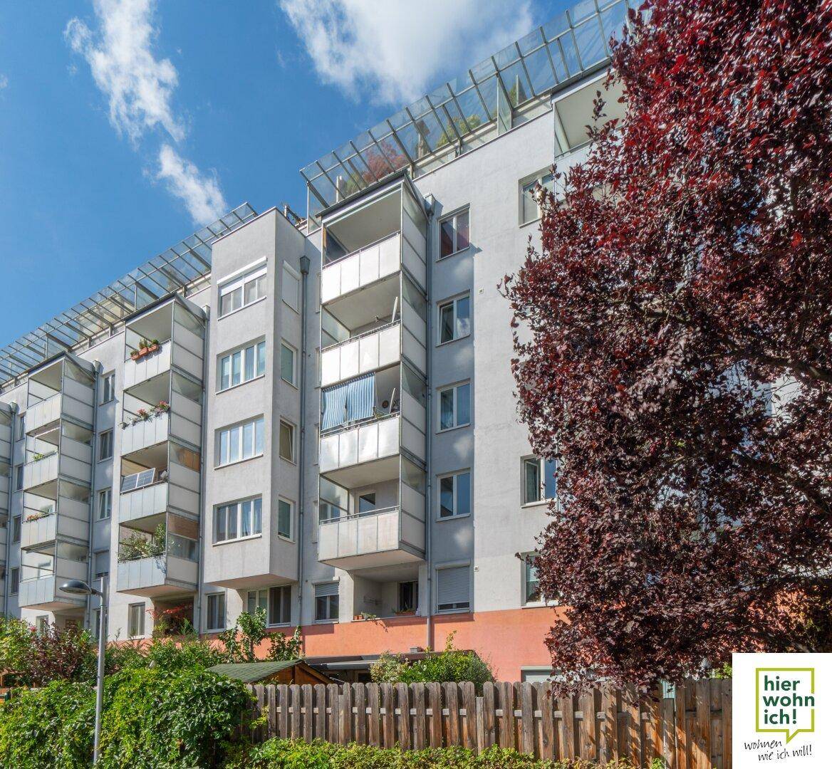 Moderne Wohnhausfassade mit zahlreichen Balkonen und großen Fenstern, umgeben von Bäumen.