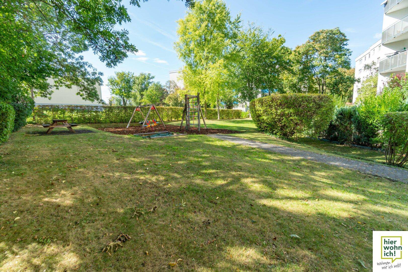 Weitläufige Grünfläche mit einem Spielplatz im Hintergrund, ideal für Familien und Kinder.