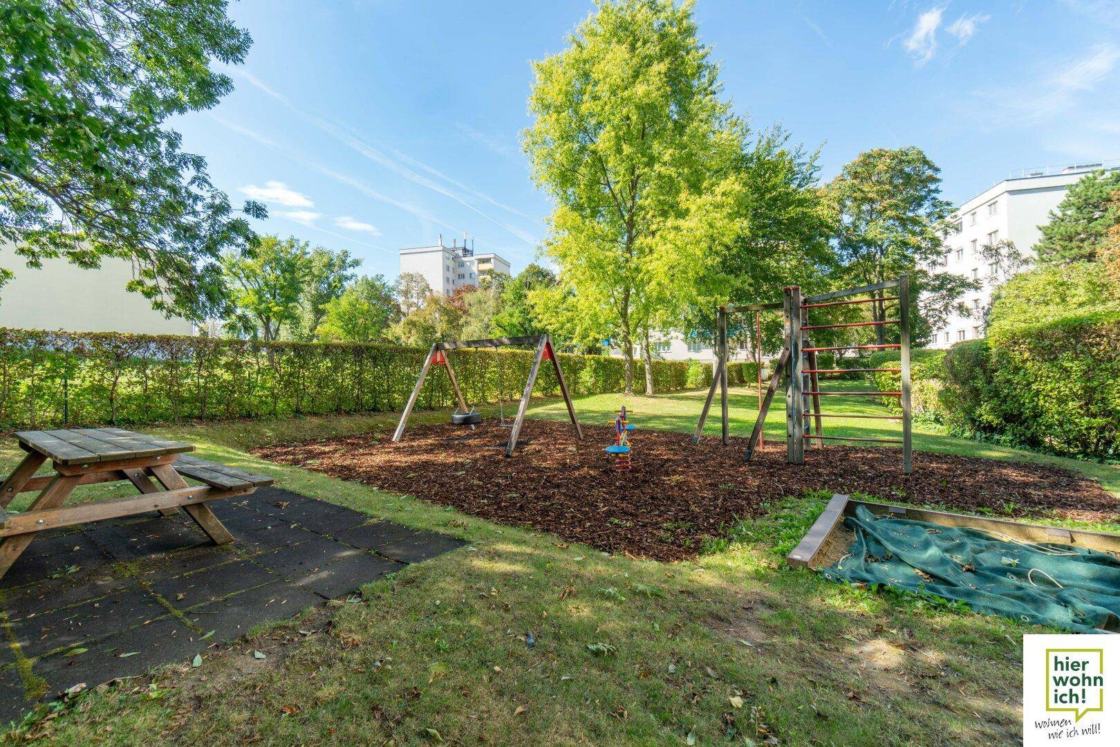 Attraktiver Spielplatz mit Picknicktisch, Schaukeln und Klettergerüst, umgeben von Bäumen.