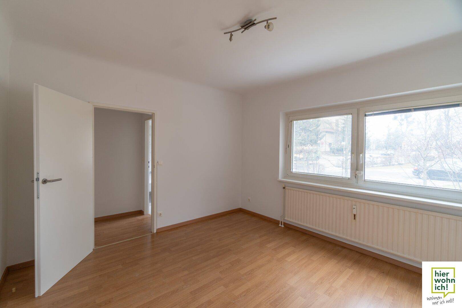Leeres Zimmer mit Holzboden, großen Fenstern und Heizkörper, bereit zur individuellen Gestaltung.