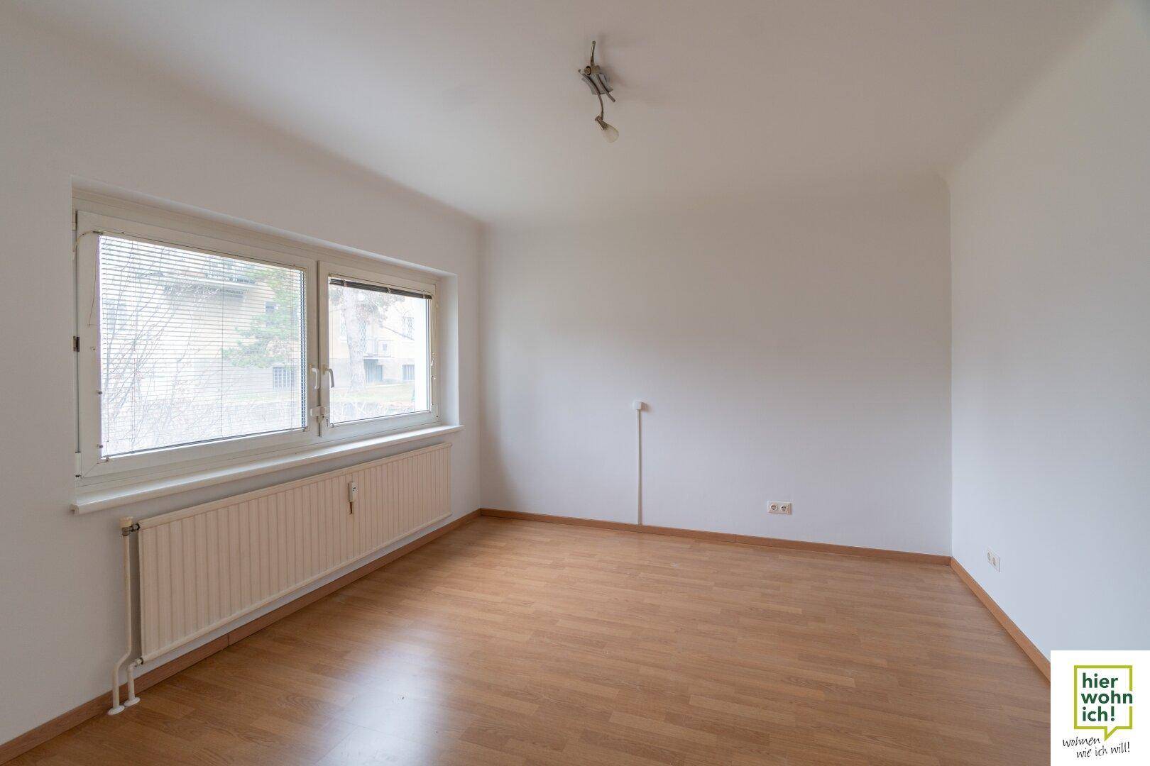 Helles, leeres Zimmer mit Holzboden und großen Fenstern, ideal für Wohn- oder Schlafbereich.