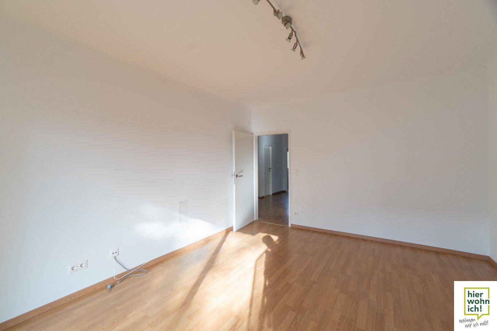 Geräumiges Wohnzimmer mit hellem Parkettboden und Zugang zu weiteren Räumen.