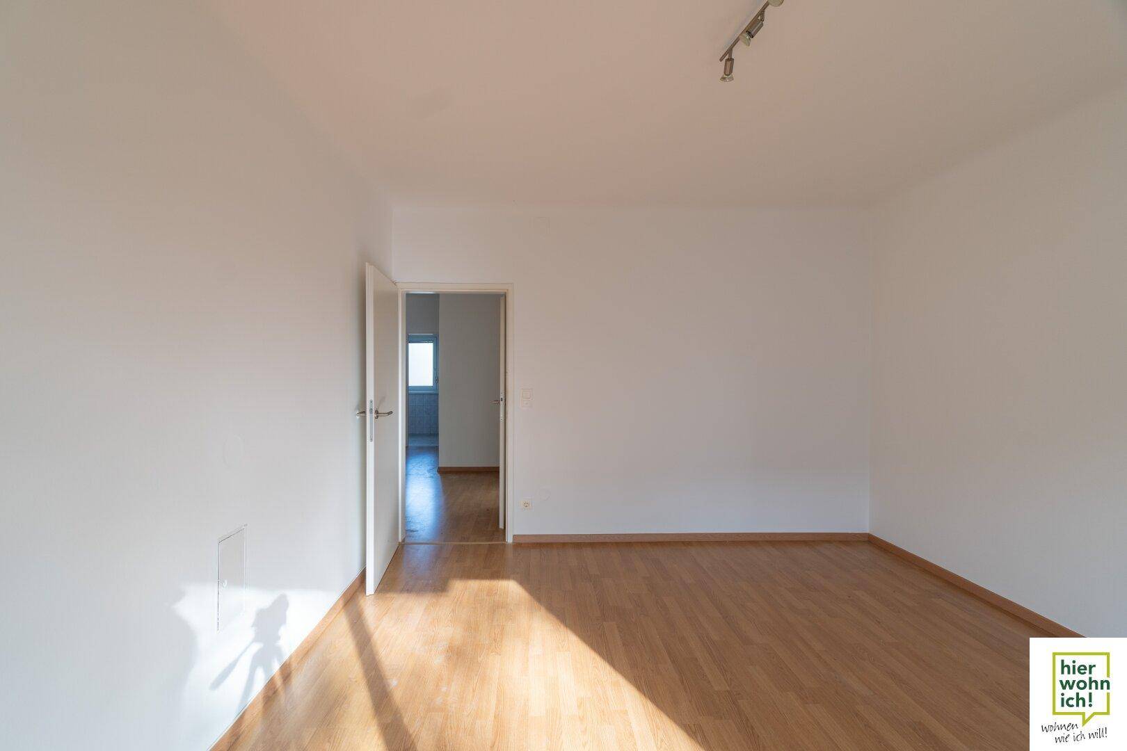 Leeres Wohnzimmer mit Parkettboden und einer Tür, die zu einem weiteren Raum führt.