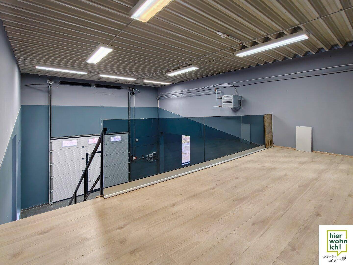 Galerieebene mit Holzboden und Glasgeländer, bietet Blick auf den darunterliegenden Gewerberaum.