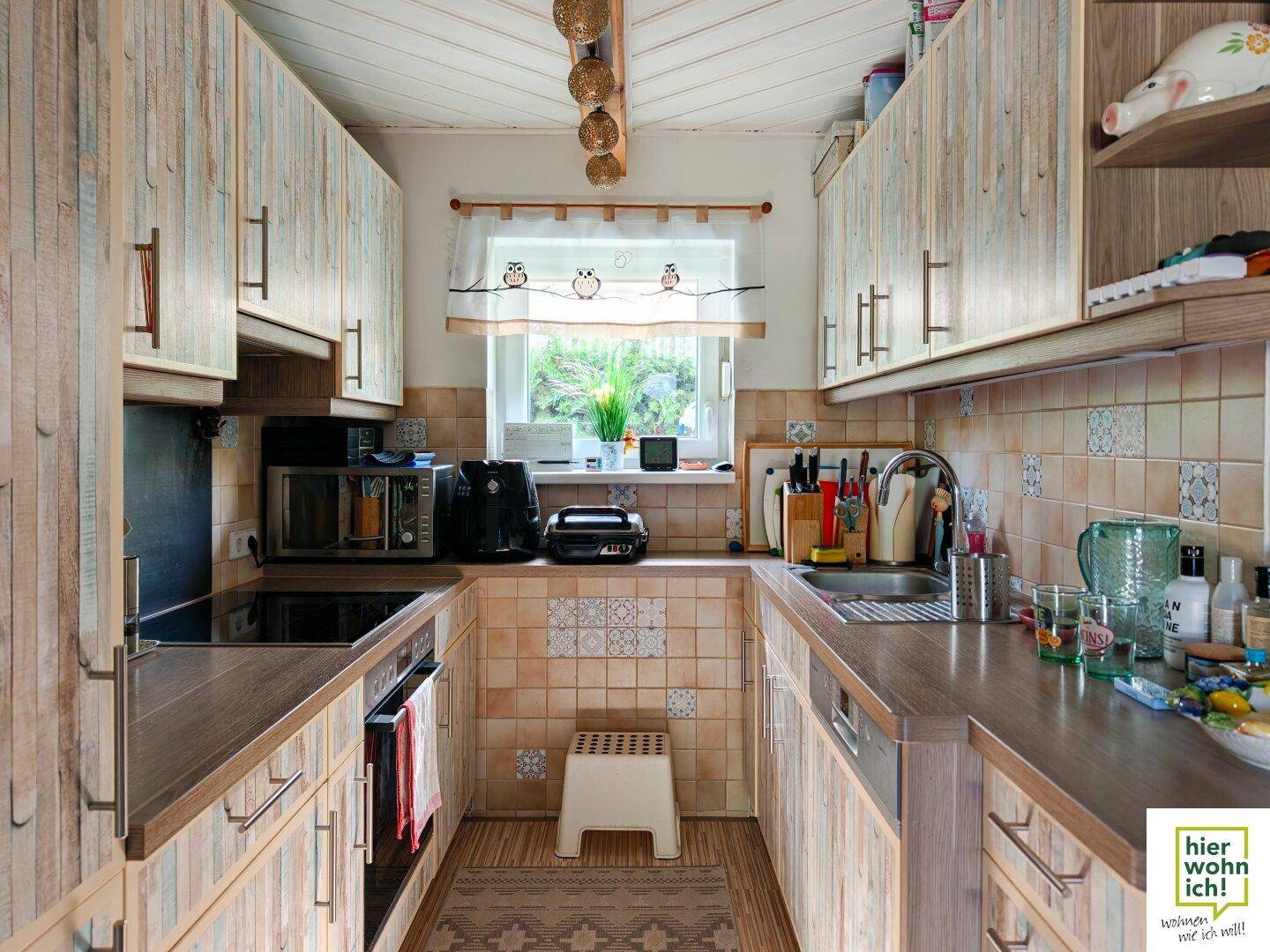 Helle Küche im Landhausstil mit Holzfronten, Fliesenboden und Blick ins Grüne.