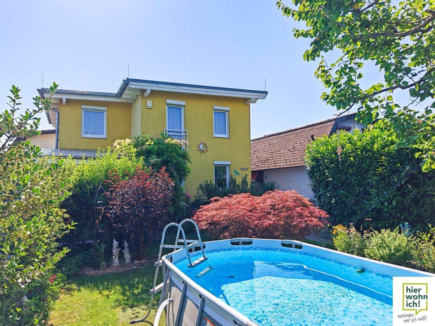 Ansicht des Hauses von hinten mit Garten, Aufstellpool und üppiger Bepflanzung.