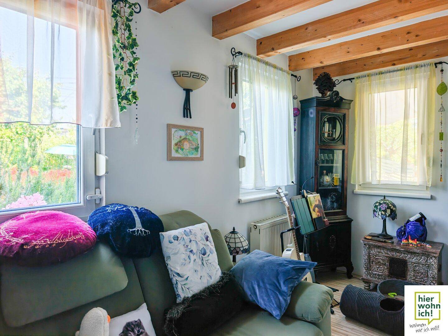 Wohnzimmer mit bequemer Couch, Holzbalken und Fenstern mit Blick ins Grüne.