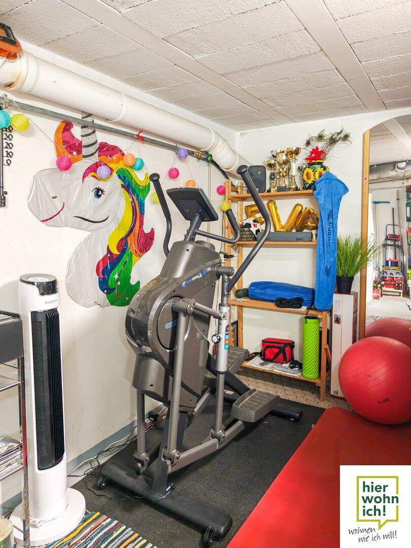 Fitnessbereich im Keller mit einem Crosstrainer und Gymnastikbällen, dekoriert mit bunten Elementen.