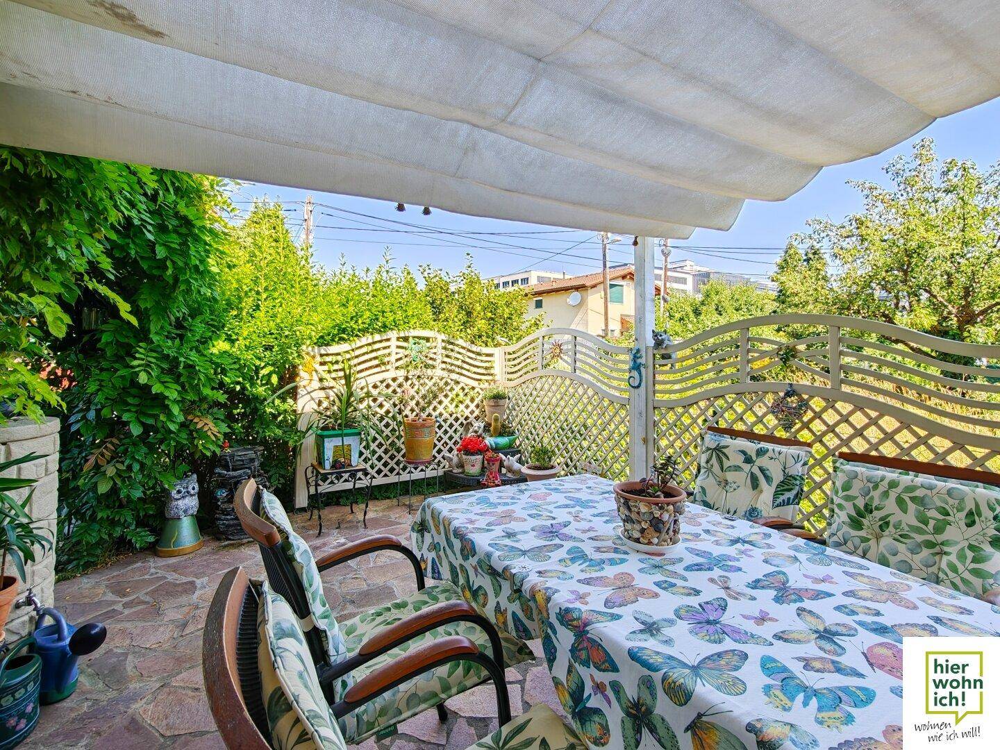 Geräumige, überdachte Terrasse mit Steinboden und Blick auf die grüne Umgebung.