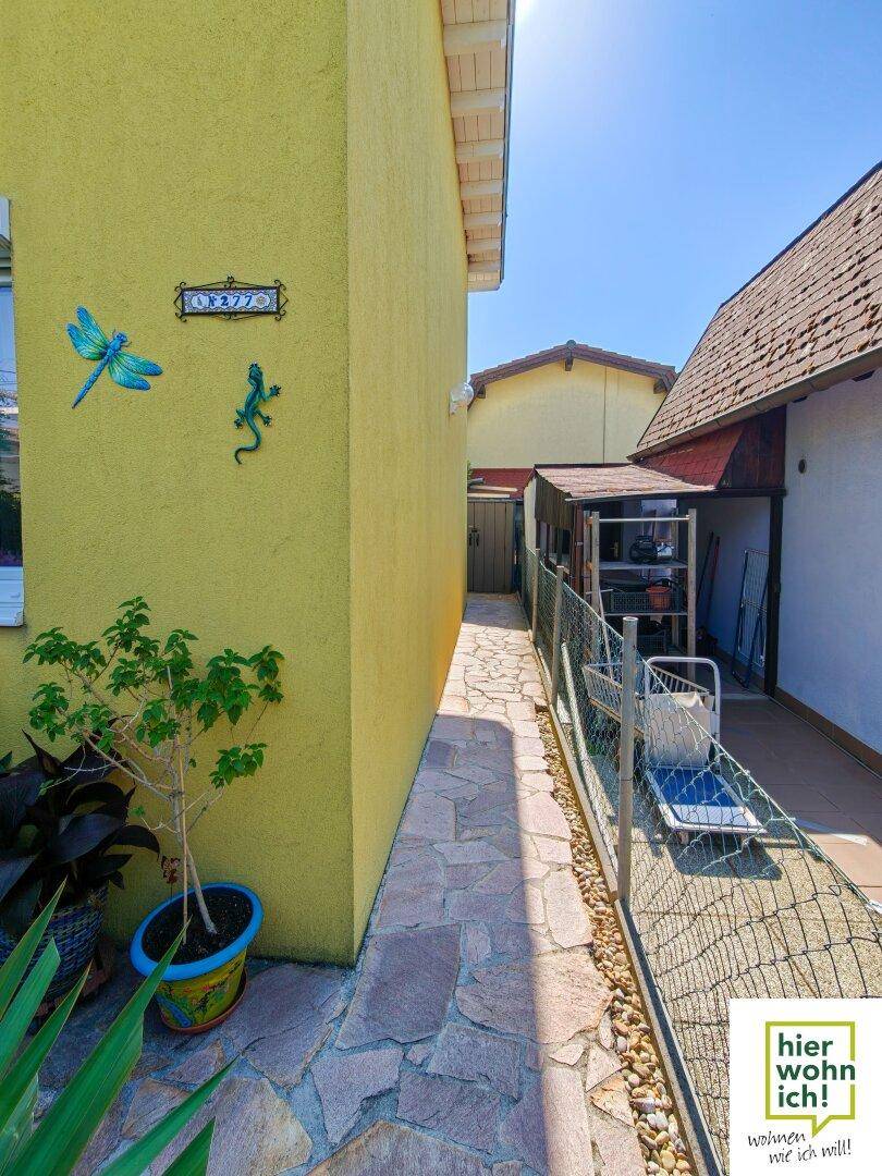 Schmaler gepflasterter Weg zwischen zwei Gebäuden mit dekorativen Elementen an der gelben Fassade.