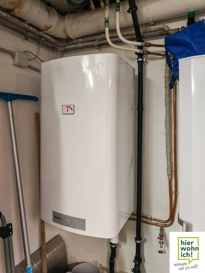 Warmwasserbereiter oder Heizkessel in einem Hauswirtschaftsraum mit sichtbaren Rohrleitungen.