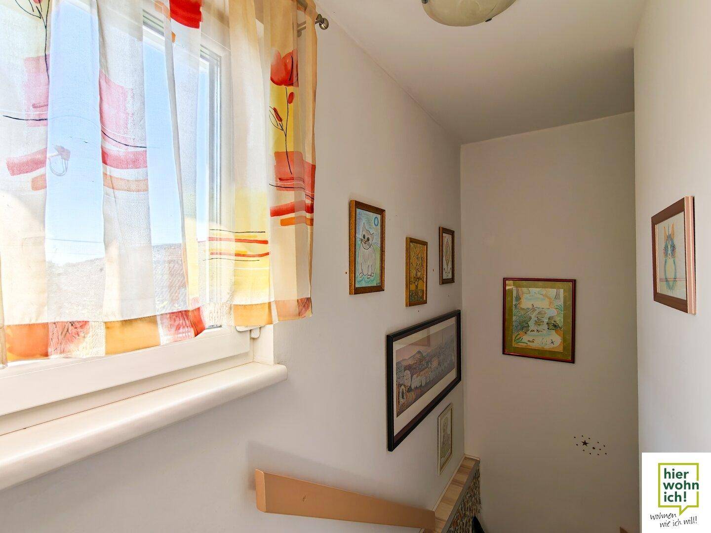 Heller Treppenabsatz mit Fenster, Bildern an der Wand und natürlichem Lichteinfall.