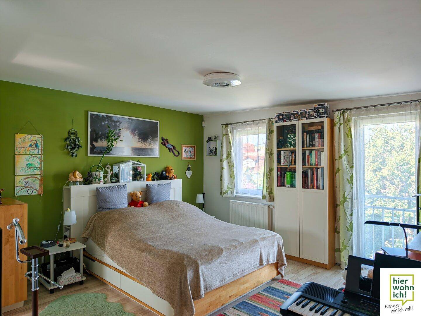 Geräumiges Schlafzimmer mit grün gestrichener Wand, Doppelbett und Zugang zum Balkon.