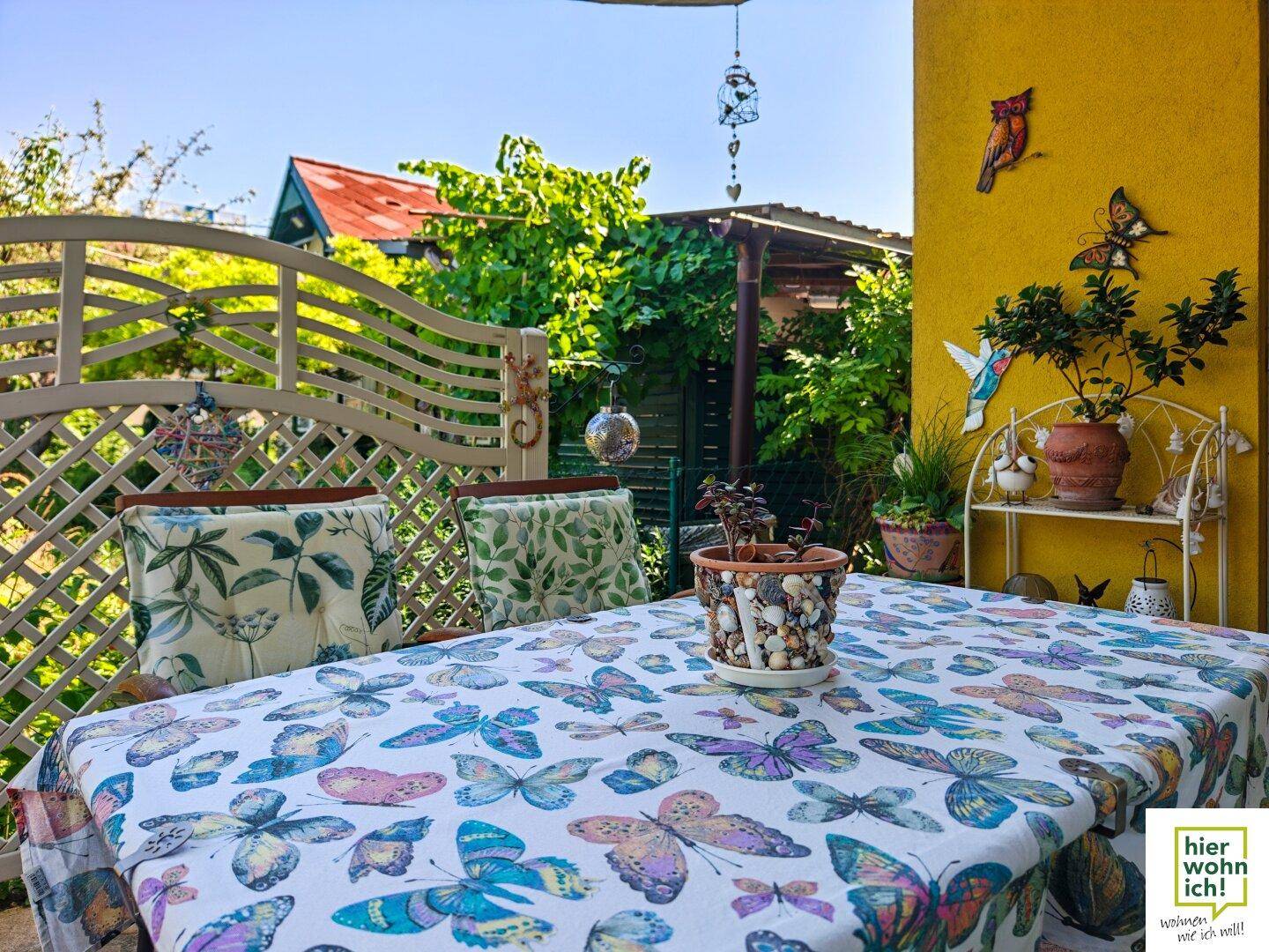 Gemütlicher Essbereich auf der Terrasse mit bunten Schmetterlingsmustern und Blick ins Grüne.