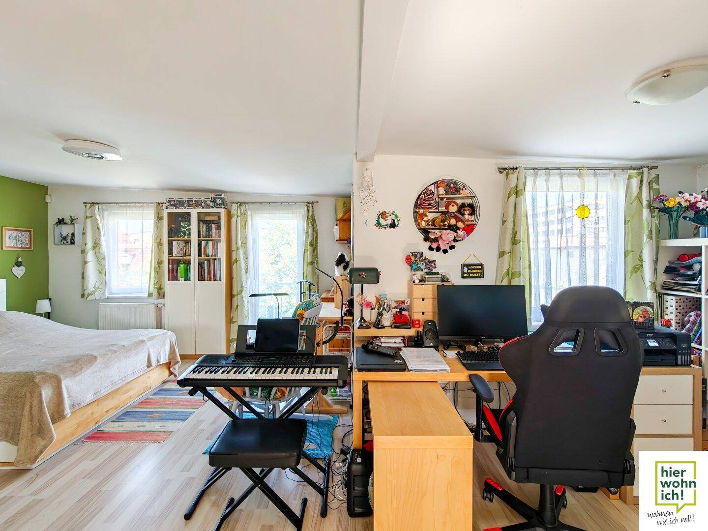 Kombiniertes Schlaf- und Arbeitszimmer mit Bett, Schreibtisch und Fenstern für natürliches Licht.
