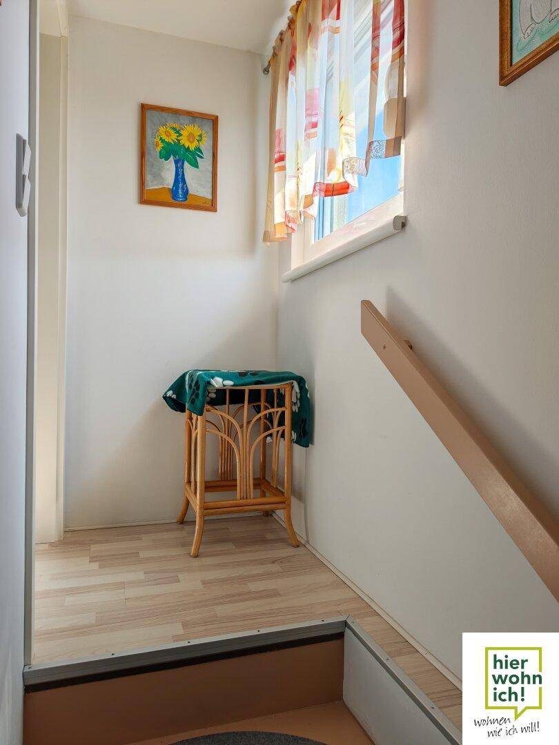 Heller Treppenabsatz mit Fenster, kleinem Beistelltisch und natürlichem Lichteinfall.