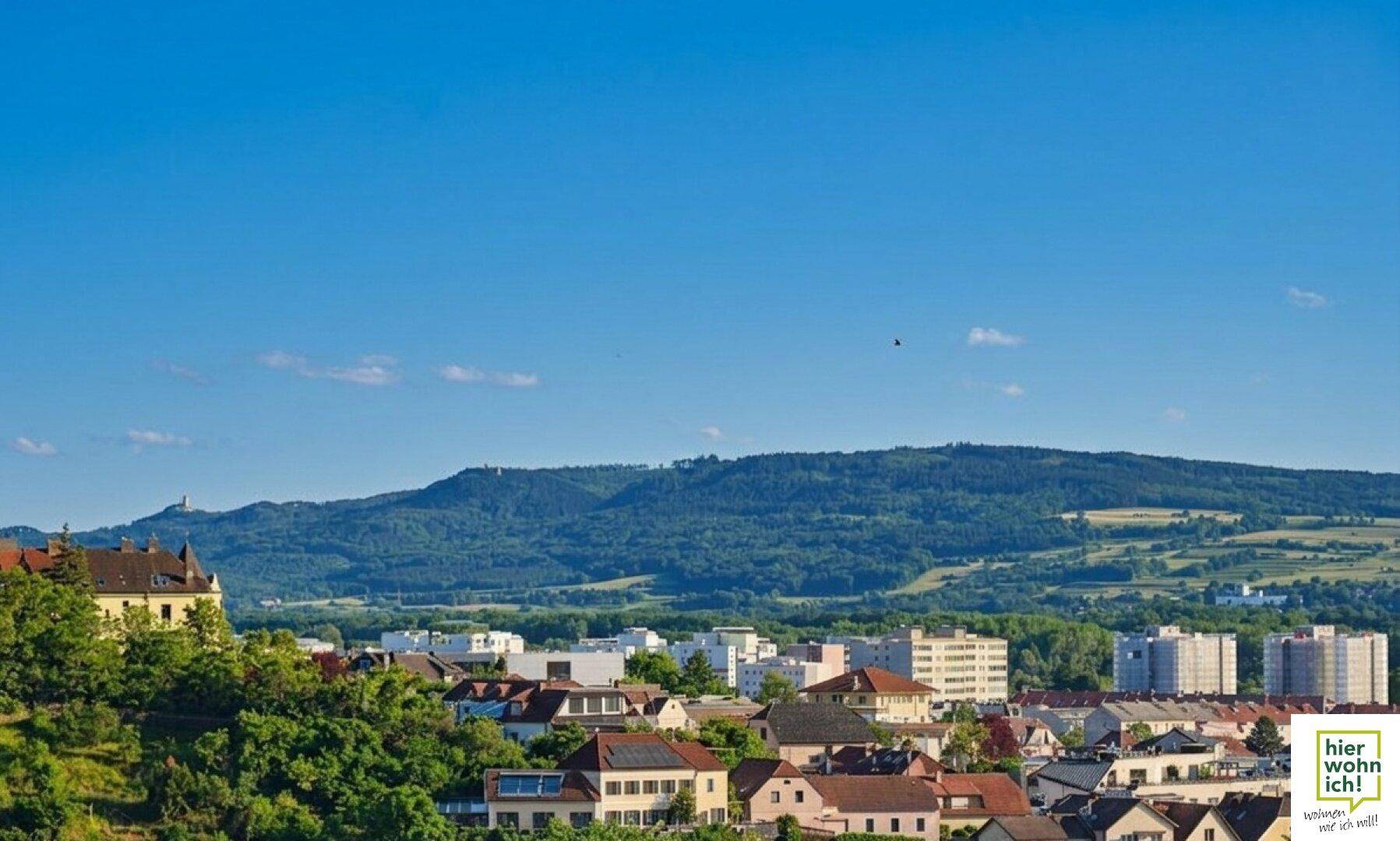 Weitblick über eine Stadt mit einer beeindruckenden Bergkette im Hintergrund unter klarem Himmel.