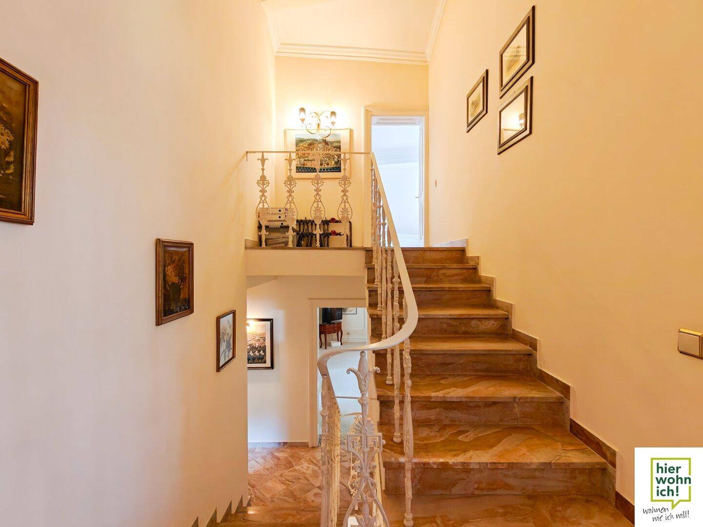 Elegantes Treppenhaus mit Marmorstufen, schmiedeeisernem Geländer und Kunstwerken.