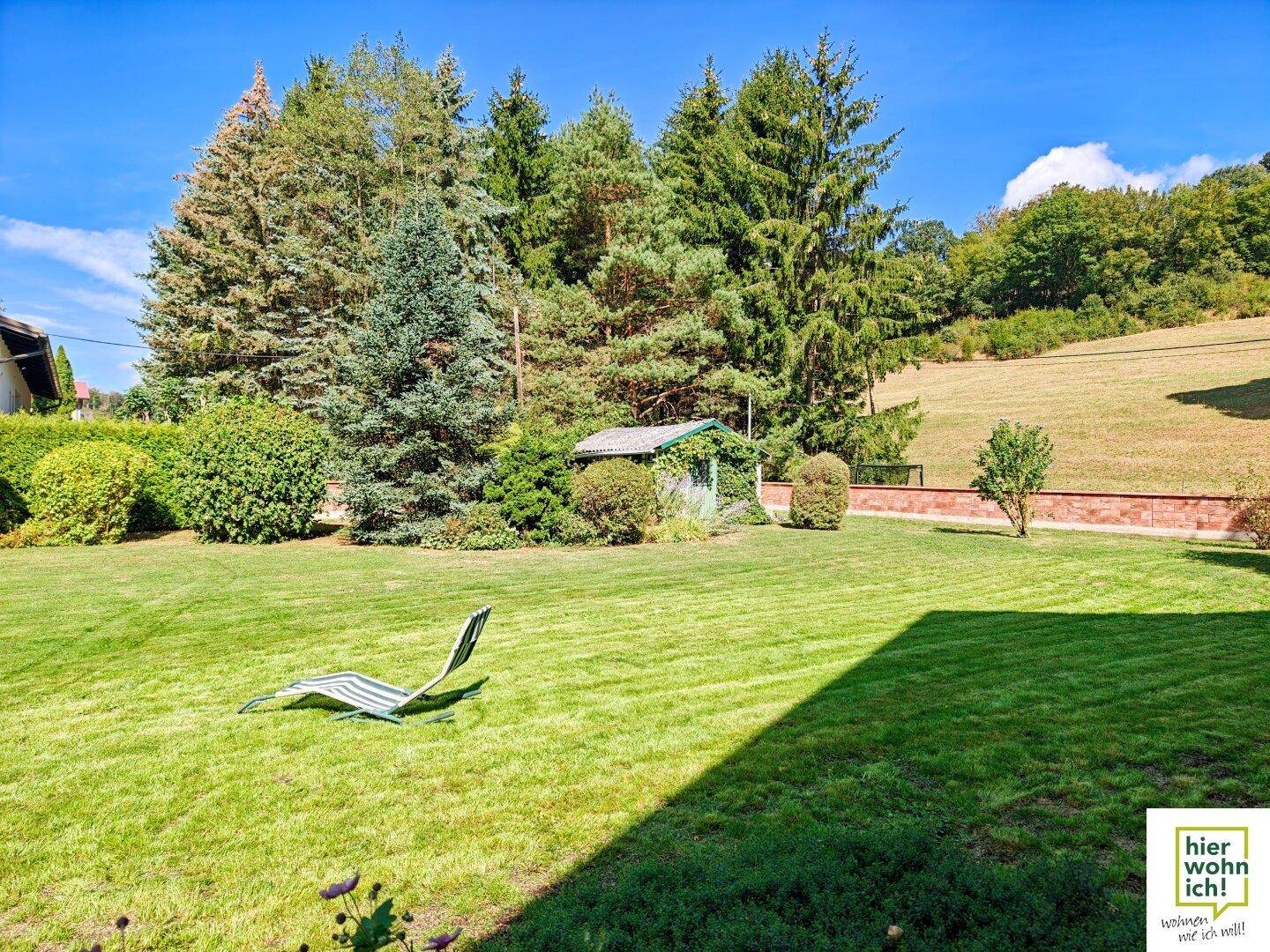 Großer, gepflegter Garten mit Rasen, umgeben von Bäumen und einem kleinen Gartenhaus.