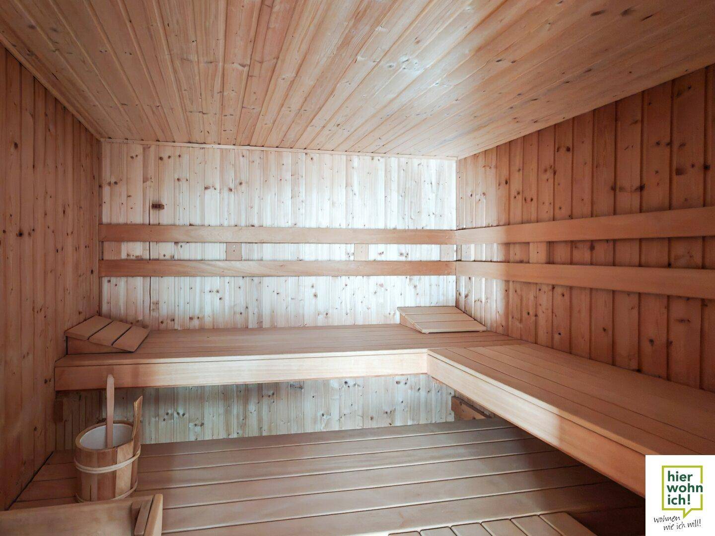 Traditionelle Holzsauna mit mehreren Bänken und einem Eimer für Aufgüsse.